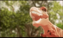 a close up of a cartoon dinosaur with its mouth open in the woods .