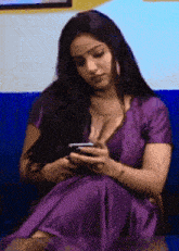 a woman in a purple dress is sitting on a blue couch and looking at her phone