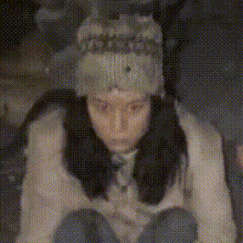 a woman wearing a hat and a sweater is sitting down in a dark room .
