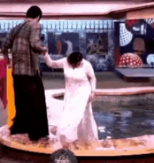 a man is holding a woman 's hand while she stands in a pool of water .