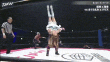 a woman is doing a handstand in a wrestling ring with a referee watching