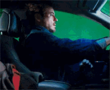 a man is sitting in the driver 's seat of a car with a green screen behind him .