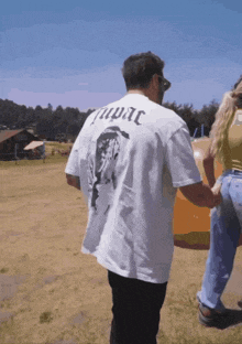 a man wearing a tupac shirt is walking with a woman