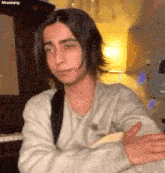 a young man with long hair is sitting in a room with his arms crossed and looking at the camera .