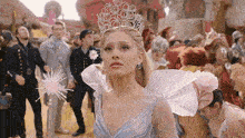 a woman in a blue dress with a crown on her head stands in front of a crowd
