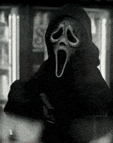 a person wearing a scream mask and a hood is holding a knife in a dark room .