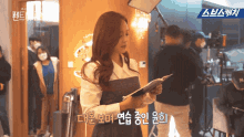 a woman in a white shirt is holding a piece of paper in front of a sign that says ' a ' on it