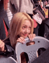 a girl with blonde hair is sitting in a chair and peeking out from behind it .