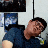 a man wearing glasses and a blue shirt is making a funny face while sitting in a chair .
