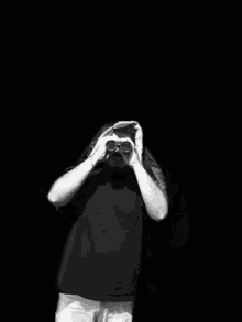 a black and white photo of a man looking through binoculars in front of a brick wall