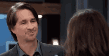 a man in a suit and a woman in a blue shirt are looking at each other and smiling .