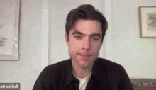 a man in a black shirt is sitting in front of a computer screen and looking at the camera .