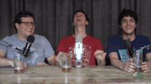three men are sitting at a table with microphones and beer
