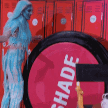 a woman with blue hair is standing in front of red lockers and a pink sign that says shade