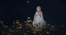 a woman in a white dress is standing in a field of flowers at night