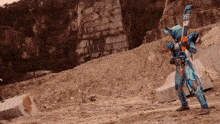 a person in a blue costume holding a brush with the letter x on it standing in a dirt field