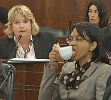 a woman is drinking from a cup while sitting at a table