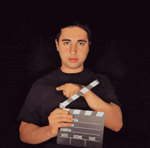 a man in a black shirt is holding a clapper board that says camera date scene and take