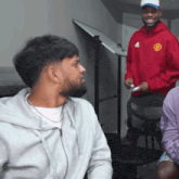 a man in a red manchester united sweatshirt smiles at another man