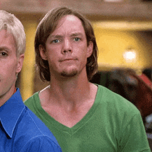 a man in a green shirt is standing next to another man in a blue shirt and looking at the camera .
