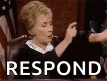 a judge is sitting at a table in a courtroom and pointing at someone .