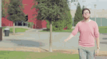 a man in a pink sweater and glasses is walking down a sidewalk .