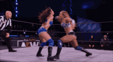 two women are wrestling in a wrestling ring while a referee watches .