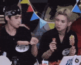 two young men are sitting at a table eating ice cream and talking to each other .