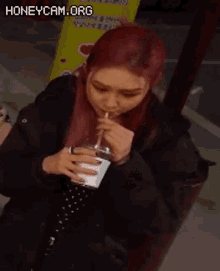 a woman with red hair is holding a glass of water with a pink straw .