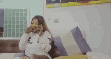 a woman is sitting on a couch talking on a cell phone while eating a meal .