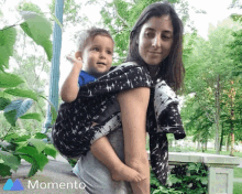 a woman carrying a child in a sling with the word momento on the bottom right