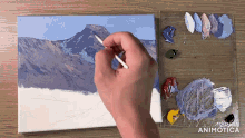 a person is painting a mountain landscape on a canvas with a palette of paint in the background