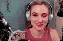 a woman wearing headphones and a red tank top smiles in front of a microphone