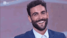 a man with a beard is smiling while wearing a suit and striped shirt .