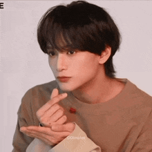 a young man is making a heart shape with his hands while wearing a brown shirt .