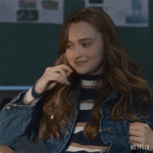 a woman in a denim jacket is covering her mouth with her hand .