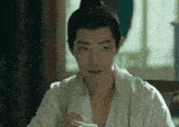 a man in a white robe is sitting at a table with a cup of tea in his hand .