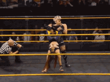 a female wrestler is doing a handstand in a wrestling ring while a referee looks on