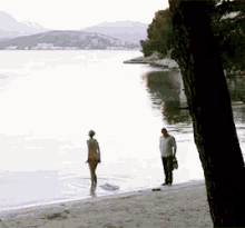 a man and a woman are standing on the beach near the water