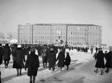 a black and white photo of a crowd of people walking in front of a building
