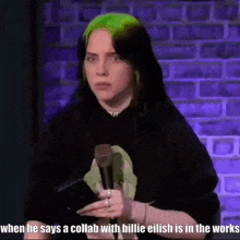 billie eilish is holding a microphone in front of a brick wall while talking about a collab