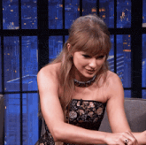 a woman in a strapless dress is sitting in front of a window with a city in the background