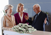 a man and two women are standing around a pile of money with one of them holding a stack of 20 dollar bills