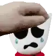 a hand is touching a stuffed animal 's head with a tear coming out of it .