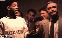 a group of people are standing around a man wearing a sweater that says l.b. blackman