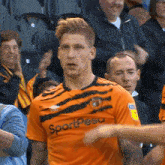 a soccer player wearing an orange shirt with the word sportpesa on it