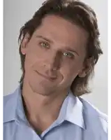 a man with long hair wearing a blue shirt smiles for the camera