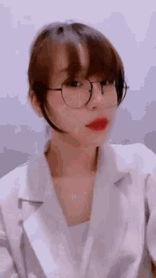 a girl wearing glasses and a white jacket is looking at the camera .