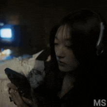 a woman wearing headphones is looking at her phone and the letters ms are on the bottom