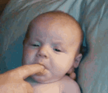 a baby is laying on a bed with a person holding his finger in his mouth .